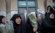 Veiled Iranian protesters hold flowers while sitting in front of effigies of Lebanon's Hez...