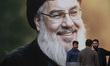 Iranian protesters stand together in front of a giant banner depicting a portrait of Leban...