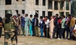 An Indian security personnel stands guard as voters queue to cast their ballots at a polli...