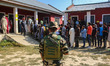 An Indian security personnel stands guard as voters queue to cast their ballots at a polli...