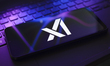 The X.AI Corp. logo appears on the screen of a smartphone that rests on top of the laptop...