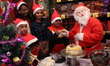 A man dressed as Santa shakes hands with a child after feeding a piece of cake following a...
