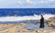 A young woman in a black coat walks along the shore of a stormy sea in Sliema, Malta, on D...