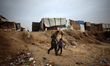 A displaced Palestinian man walks in front of tents with his son while pulling a donkey ne...