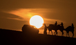 People ride on a camel along the Sealine Sand Dunes against the backdrop of the last sunse...