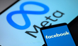 Facebook is displayed on a mobile phone with the Meta logo visible on a tablet screen in t...