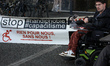 A disabled man stands near a banner reading 'Stop handiphobia' and 'Nothing for us, withou...