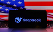 Deepseek logo is screened on a mobile phone with US flag in the background for illustratio...