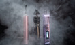 Three vaping e-cigarette devices are visible with smoke around them. 