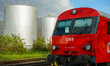 A red OBB (Austrian Federal Railways) train is stationed near large silver industrial stor...