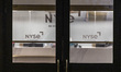 Side entrance of NYSE with a screen showing the stocks and the NYSE logo. Night view of th...