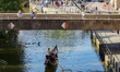 A gondolier rows a gondola with a passenger beneath a pedestrian bridge on a canal in Bamb...