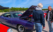 A purple Dodge Charger R/T has its hood open while visitors discuss the vehicle during the...
