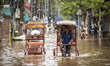 Commuters in cycle rickshaws wade through a flooded street after heavy rains in Guwahati,...