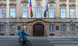 A bicycle food courier rides through a historic street with Czech and EU flags in Prague,...