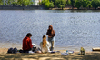 Three young people spend time together on the sandy bank of the Vltava River, sketching an...