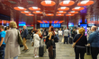 A large number of passengers stand with luggage in front of the departure boards in the ma...