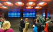 A large number of passengers stand with luggage in front of the departure boards in the ma...