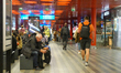 People sit and walk in the main corridor of Prague Central Station, surrounded by signage,...