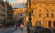 Evening sunlight illuminates the facade of the National Theatre while pedestrians, cyclist...