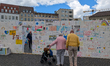 Elderly visitors examine a colorful wall of peace filled with multilingual drawings and me...