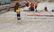 Construction workers operate heavy tools and position reinforcement materials on a concret...