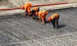 Construction workers operate heavy tools and position reinforcement materials on a concret...