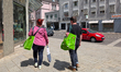 Two people walk in the city carrying green reusable shopping bags from the Asian supermark...