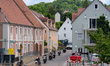 A group of motorcyclists rides through a narrow residential street near a construction zon...