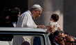Pope Leo XIV holds a baby as he arrives in the popemobile for the weekly general audience...