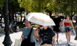 Tourists use umbrellas to protect from the sun during warm weather in the center of Athens...