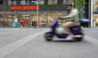 A man on a purple scooter passes by the Woolworth retail store as people enter and exit th...