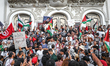 Pro-Palestinian demonstrators wave Tunisian and Palestinian flags while holding a sign rea...