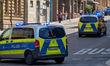 Police vehicles with flashing blue lights respond on an urban road during an active operat...