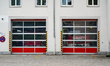 A fire brigade station with red fire brigade vehicles and closed garage gates displays vis...