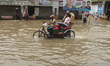 Local transport tries to drive and people wade through a waterlogged street after heavy ra...