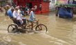 Local transport tries to drive and people wade through a waterlogged street after heavy ra...