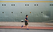 A man jogs along the street next to a cruise ship docked in Rotterdam Harbor in Rotterdam,...