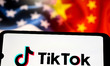 The TikTok logo appears on a smartphone screen, with the American and Chinese flags shown...