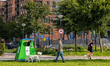 A man walks his dog past a green plastic recycling container while two joggers run nearby...