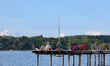 People sit and stand on a wooden pier by Lake Ammersee in Herrsching, Bavaria, Germany, on...