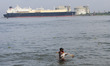 A fisherman casts his fishing nets into the waters of the Arabian Sea with the LNG Tanker...