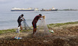 Fishermen arrange their fishing at a seashore with the LNG Tanker British Mentor anchored...