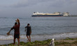 Fishermen arrange their fishing at a seashore in the backdrop of LNG Tanker British Mentor...