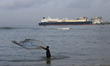 A fisherman casts his fishing nets into the waters of the Arabian Sea with the LNG Tanker...