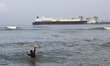 A fisherman casts his fishing nets into the waters of the Arabian Sea with the LNG Tanker...