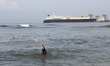 A fisherman casts his fishing nets into the waters of the Arabian Sea with the LNG Tanker...