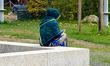 A woman sits on a stone bench and uses her smartphone in a park in Neumarkt in der Oberpfa...