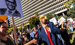 A Trump impersonator greets a protester with a George Santos sign as thousands rally and m...