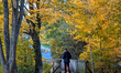 A senior citizen walks with the help of walking sticks along a leaf-covered path surrounde...